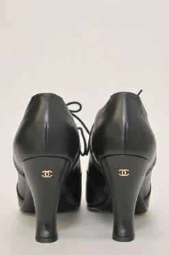 Black brogued leather pointed-toe lace-up Victorian-style heeled booties with metallic Coco Mark heel plaque appliqué