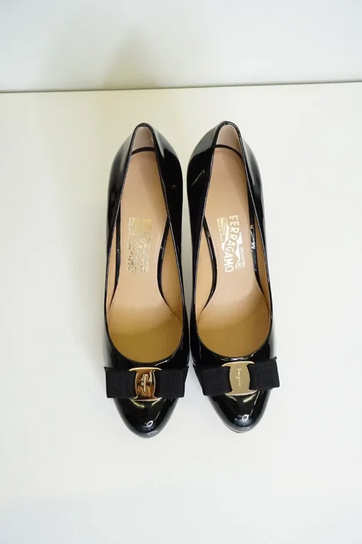 Black patent platform pumps with grosgrain Vara bow wrapped in brand's signature engraved metal plaque