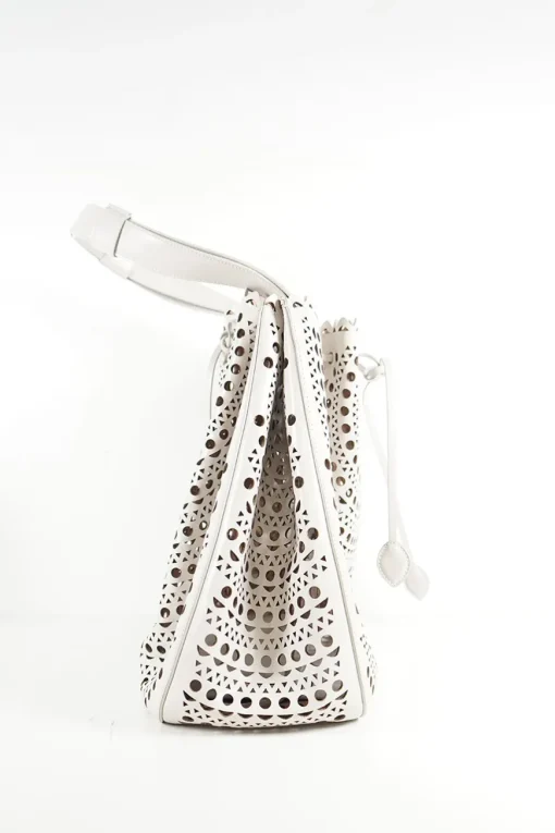 Grey perforated leather top handle bag. Drawstring closure. Bag comes with detachable leather zip pouch