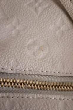 Louis Vuitton Empreinte monogram embossed calf leather bag in cream colour with zip closure. Rectangular shape with 2 shoulder straps. Bag has one external zipped pocket. Interior is fabric lined, with two side pockets, and a third on front panel. Gold toned hardware.