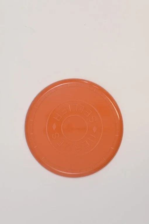 Orange plastic Wouf flying disc featuring 'Hermès Sellier Paris' embossed detail