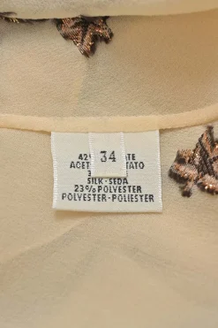 Beige embroidered silk-blend high collar keyhole-front blouse featuring trapeze artist novelty motif