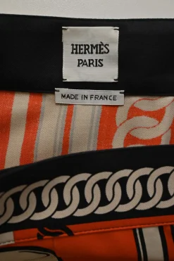 Coral and black silk chainlink foulard print apron-style pleated mini skirt with horsebit-trimmed waist
