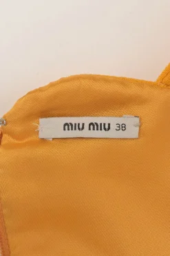 Mustard yellow bow-embellished wool pinafore mini dress featuring metallic floral appliqué and slanted hip pockets